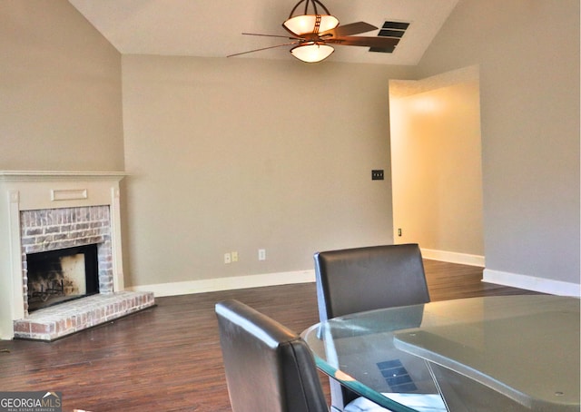 dining area with ceiling fan, vaulted ceiling, a fireplace, and dark wood-type flooring