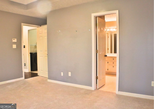 unfurnished bedroom featuring washer / dryer, light colored carpet, and ensuite bath