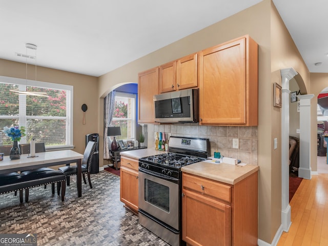 kitchen with pendant lighting, backsplash, appliances with stainless steel finishes, and hardwood / wood-style floors