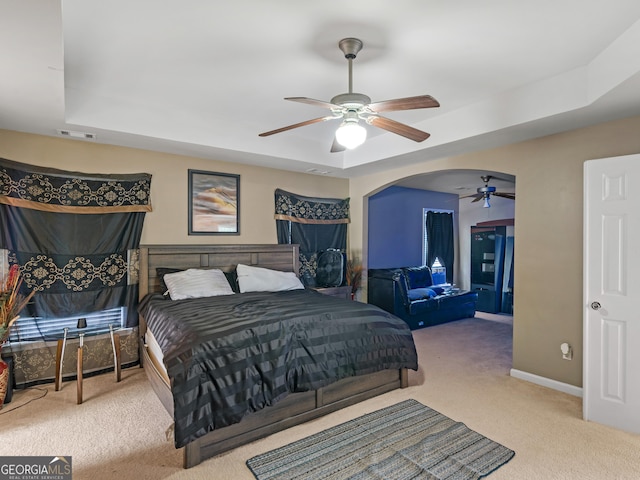 bedroom featuring ceiling fan, light colored carpet, and a tray ceiling