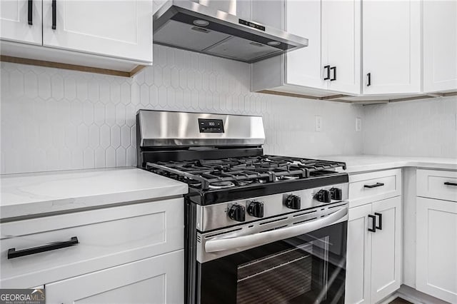 kitchen with tasteful backsplash, white cabinets, stainless steel gas range, and wall chimney range hood