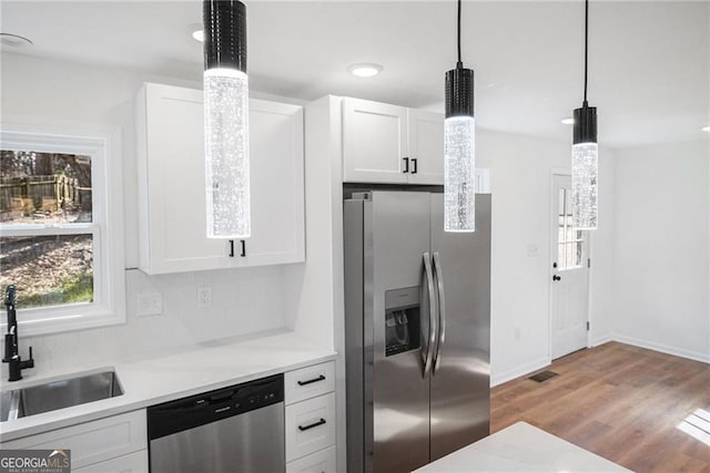 kitchen featuring sink, white cabinetry, hanging light fixtures, appliances with stainless steel finishes, and hardwood / wood-style floors