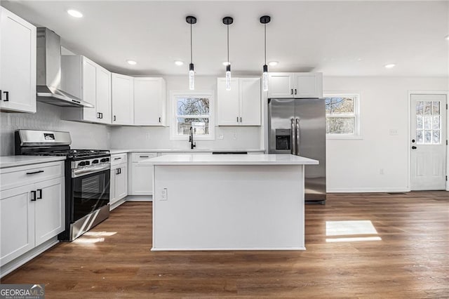 kitchen with wall chimney exhaust hood, appliances with stainless steel finishes, decorative light fixtures, and white cabinets