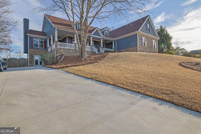 view of front of house with a porch, stone siding, driveway, a gate, and a chimney