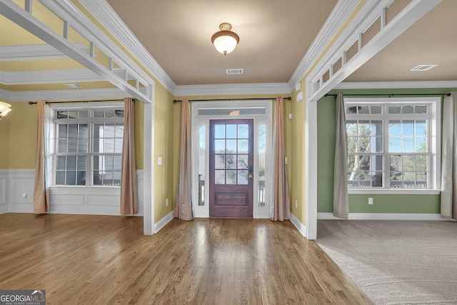 entryway with visible vents, ornamental molding, a decorative wall, and wood finished floors