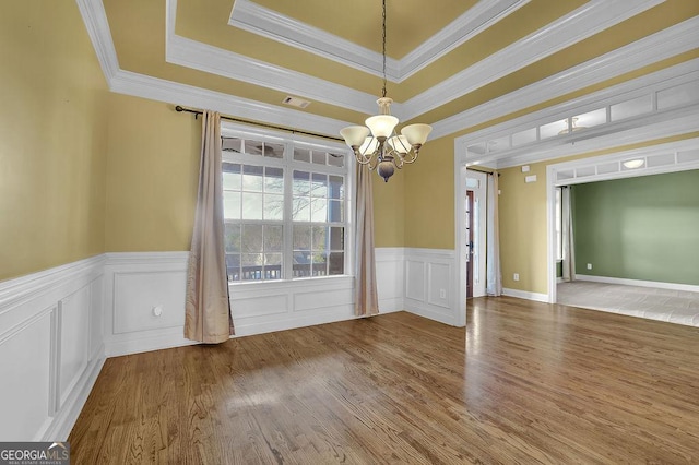 unfurnished dining area with a wainscoted wall, wood finished floors, visible vents, a raised ceiling, and an inviting chandelier