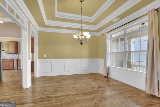 unfurnished dining area with visible vents, a wainscoted wall, wood finished floors, an inviting chandelier, and a tray ceiling