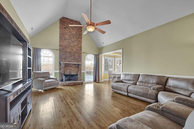 living area featuring ceiling fan, high vaulted ceiling, a fireplace, wood finished floors, and visible vents