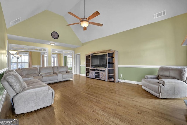 living area featuring high vaulted ceiling, visible vents, wood finished floors, and ceiling fan with notable chandelier