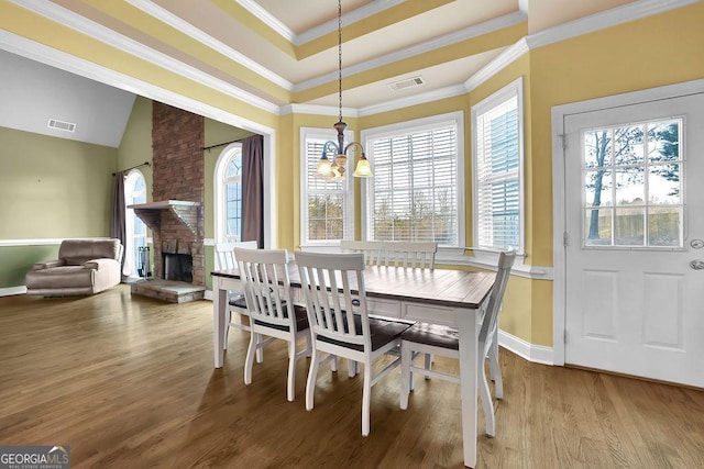 dining space with a chandelier, a brick fireplace, ornamental molding, and hardwood / wood-style flooring