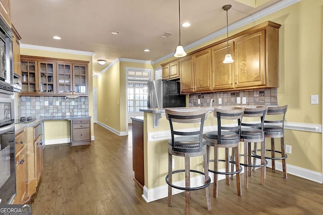 kitchen featuring brown cabinetry, a kitchen bar, freestanding refrigerator, and crown molding