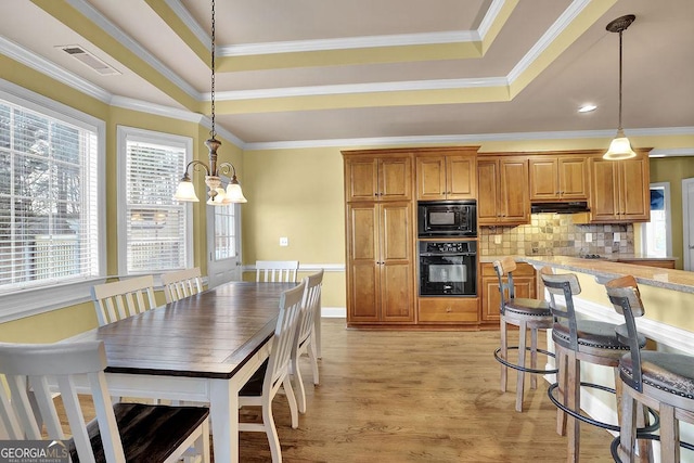 kitchen with a tray ceiling, visible vents, decorative backsplash, brown cabinetry, and black appliances