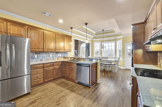 kitchen with stainless steel appliances, a sink, backsplash, brown cabinetry, and a raised ceiling