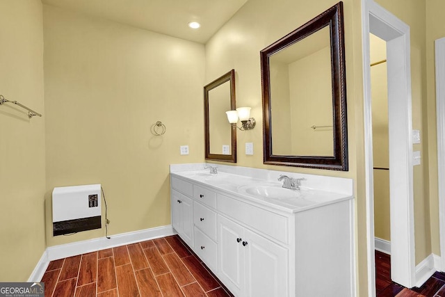 bathroom with heating unit, a sink, baseboards, wood tiled floor, and double vanity