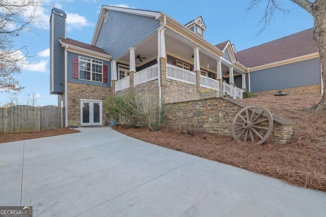 view of front of home with stone siding, a chimney, a ceiling fan, and french doors