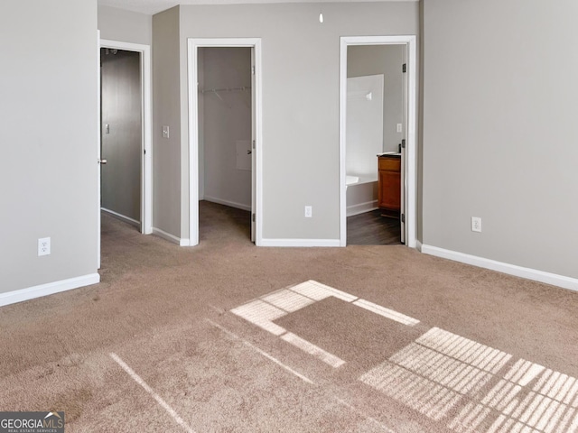 unfurnished bedroom with a spacious closet, ensuite bathroom, a closet, and carpet flooring