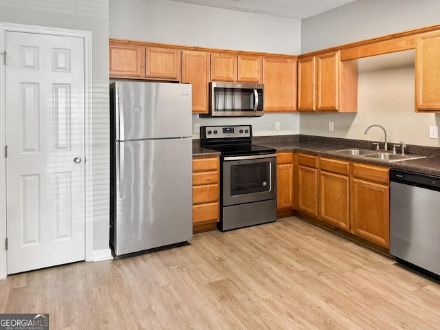 kitchen featuring a textured ceiling, appliances with stainless steel finishes, light wood-type flooring, and sink