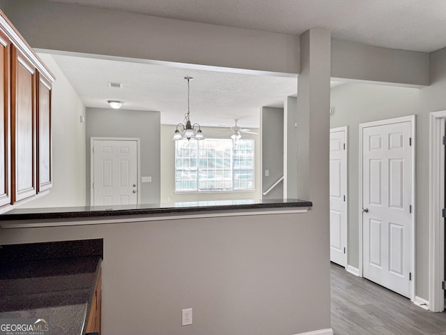 kitchen featuring a textured ceiling, pendant lighting, ceiling fan with notable chandelier, and wood-type flooring