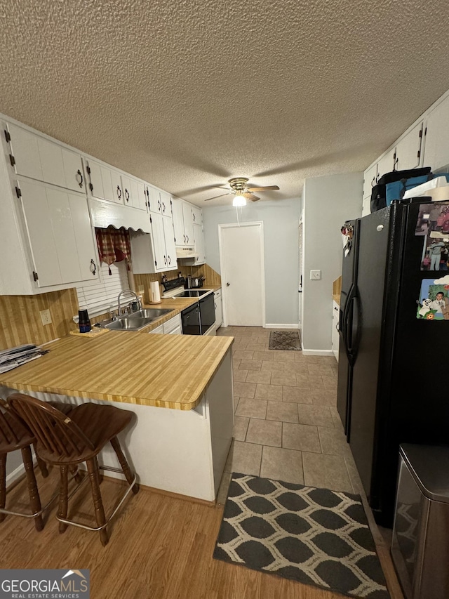 kitchen with sink, a breakfast bar area, white cabinetry, black refrigerator with ice dispenser, and kitchen peninsula