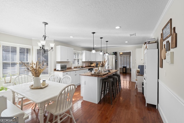 kitchen with pendant lighting, a center island, butcher block countertops, sink, and white cabinetry