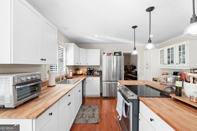 kitchen featuring stainless steel appliances, butcher block counters, white cabinets, and hanging light fixtures