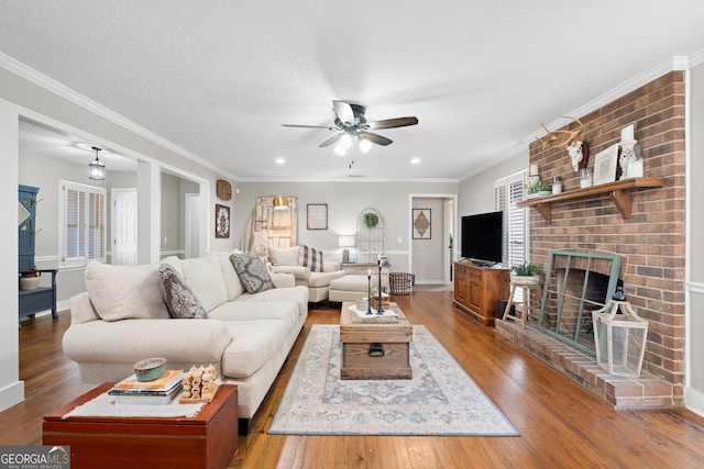 living room with a textured ceiling, wood-type flooring, a fireplace, ceiling fan, and crown molding