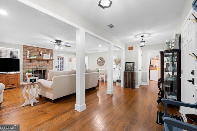 living room featuring ceiling fan, wood-type flooring, a brick fireplace, and a textured ceiling