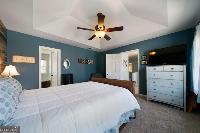 carpeted bedroom featuring ceiling fan, a raised ceiling, and ensuite bath