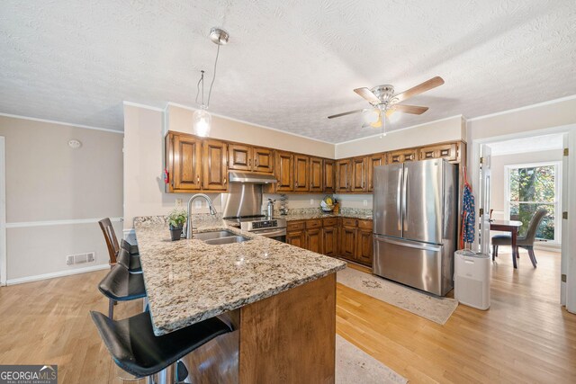 kitchen featuring light wood-type flooring, hanging light fixtures, kitchen peninsula, stainless steel appliances, and a textured ceiling