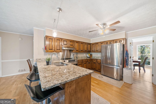 kitchen featuring a kitchen bar, sink, hanging light fixtures, appliances with stainless steel finishes, and kitchen peninsula