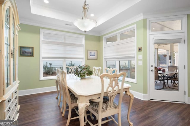 dining area featuring dark wood-type flooring, a tray ceiling, ornamental molding, and a healthy amount of sunlight