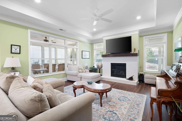 living room with a fireplace, dark hardwood / wood-style floors, ceiling fan, a tray ceiling, and crown molding