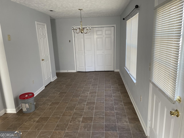 unfurnished dining area featuring a textured ceiling, baseboards, and an inviting chandelier