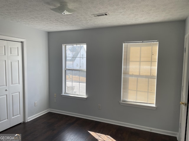 unfurnished bedroom with a textured ceiling, visible vents, baseboards, a closet, and dark wood-style floors