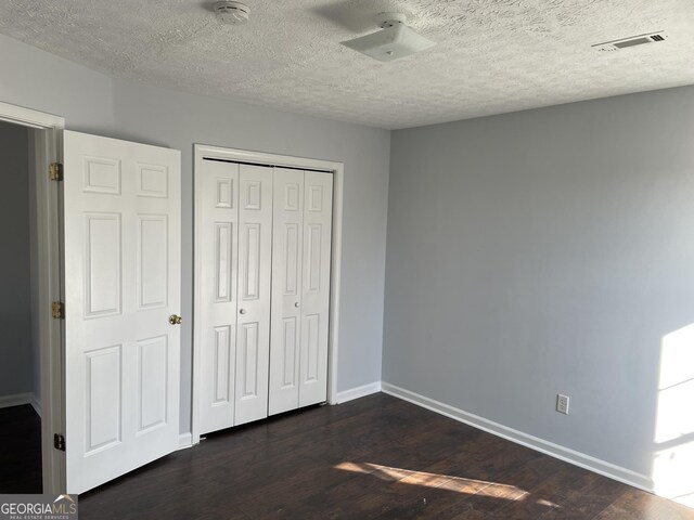 unfurnished bedroom featuring a closet, dark hardwood / wood-style flooring, and a textured ceiling