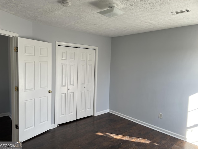 unfurnished bedroom with baseboards, visible vents, dark wood-type flooring, a textured ceiling, and a closet