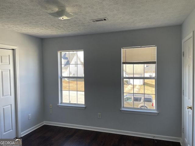 spare room with dark wood finished floors, visible vents, plenty of natural light, and baseboards