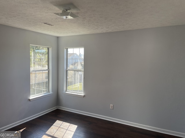 empty room featuring visible vents, a textured ceiling, baseboards, and dark wood-type flooring