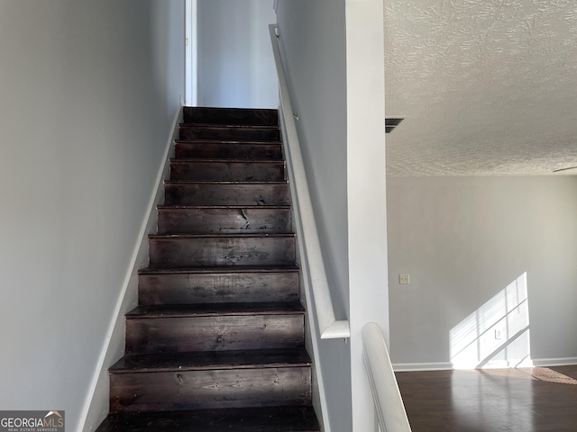 staircase with a textured ceiling and wood-type flooring