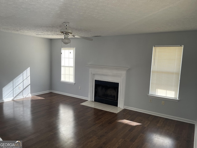 unfurnished living room with a textured ceiling, wood finished floors, a fireplace with flush hearth, a ceiling fan, and baseboards