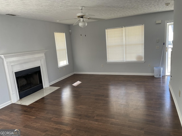 unfurnished living room with ceiling fan, wood finished floors, a fireplace with flush hearth, visible vents, and baseboards