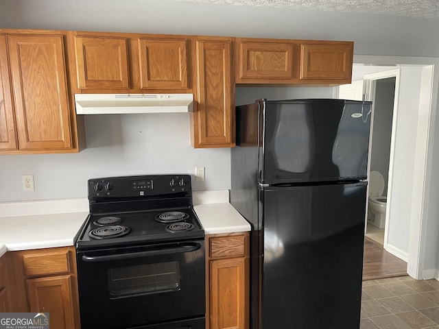 kitchen with brown cabinets, black appliances, under cabinet range hood, and light countertops