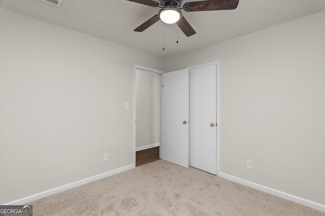 unfurnished bedroom featuring ceiling fan, light carpet, and a textured ceiling