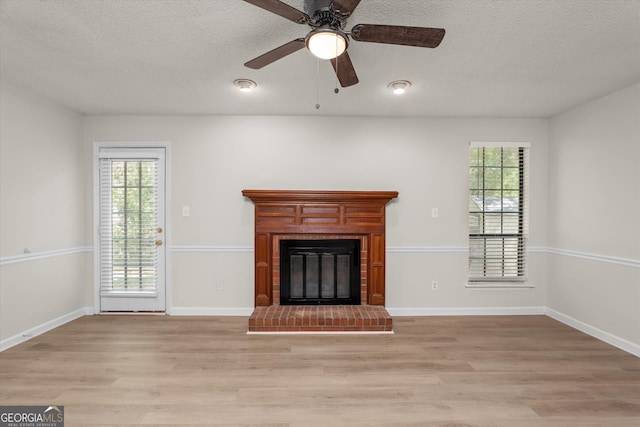 unfurnished living room featuring a textured ceiling, a brick fireplace, light hardwood / wood-style flooring, and ceiling fan