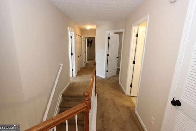 hallway with a textured ceiling and light carpet