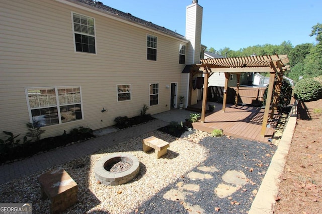 back of house with a pergola, a wooden deck, and an outdoor fire pit