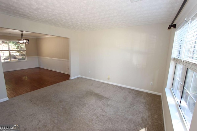 unfurnished room featuring plenty of natural light, a textured ceiling, a notable chandelier, and dark colored carpet