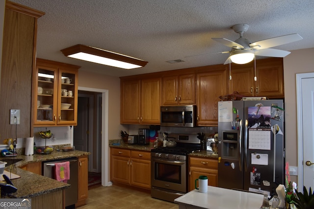 kitchen with appliances with stainless steel finishes, brown cabinets, glass insert cabinets, and a textured ceiling