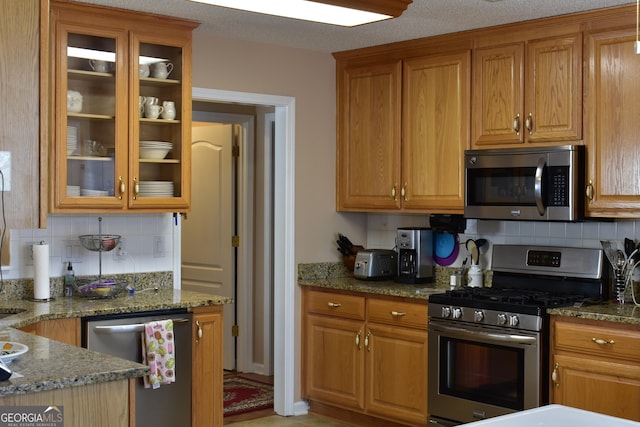 kitchen with glass insert cabinets, stone countertops, appliances with stainless steel finishes, and brown cabinetry