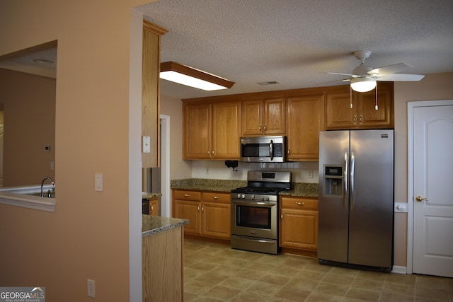 kitchen with ceiling fan, a textured ceiling, stainless steel appliances, visible vents, and brown cabinetry